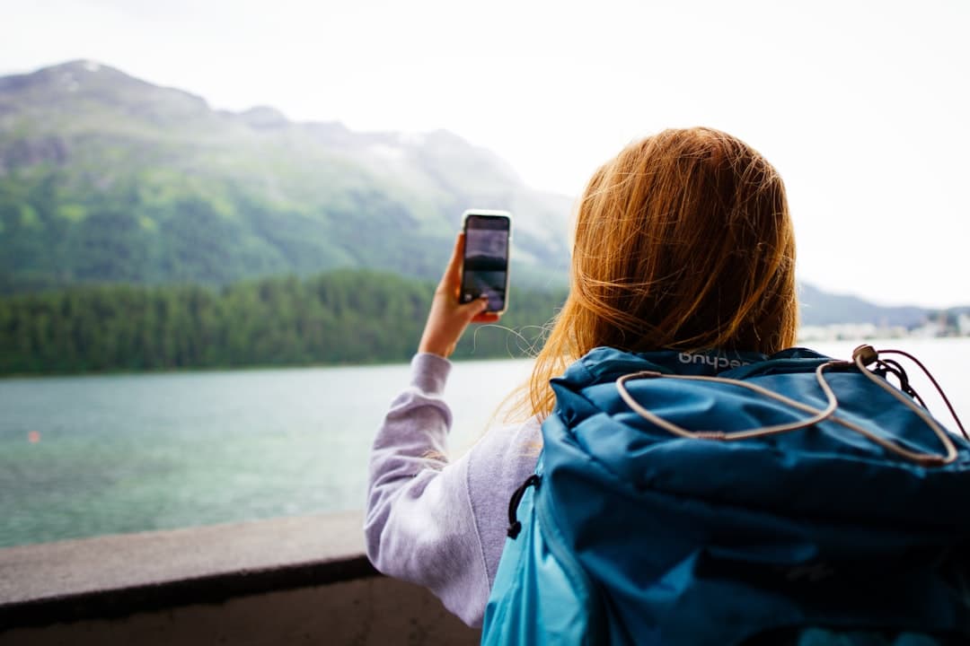 Voyageuse avec sac à dos tenant son smartphone face à un lac de montagne